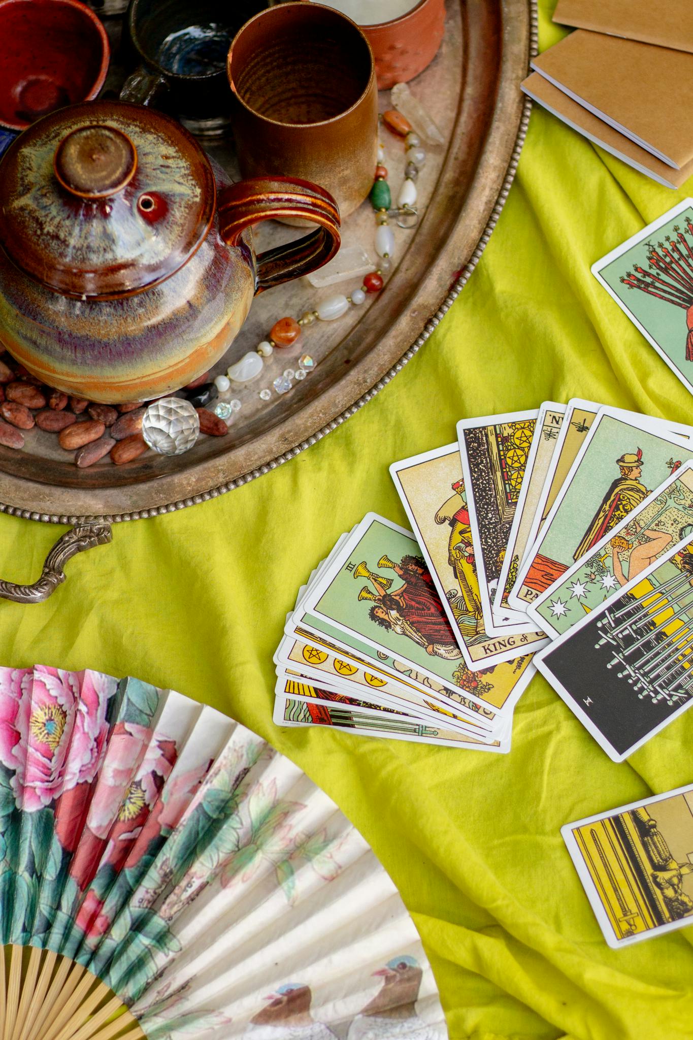 A vibrant tarot reading setup with pottery, fan, and tarot cards arranged on a bright cloth.